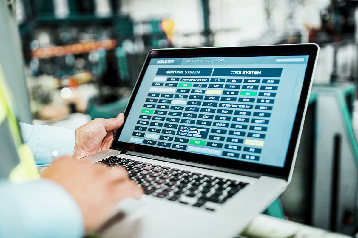 Person am Laptop mit Produktionssteuerung in einer Fertigungshalle.