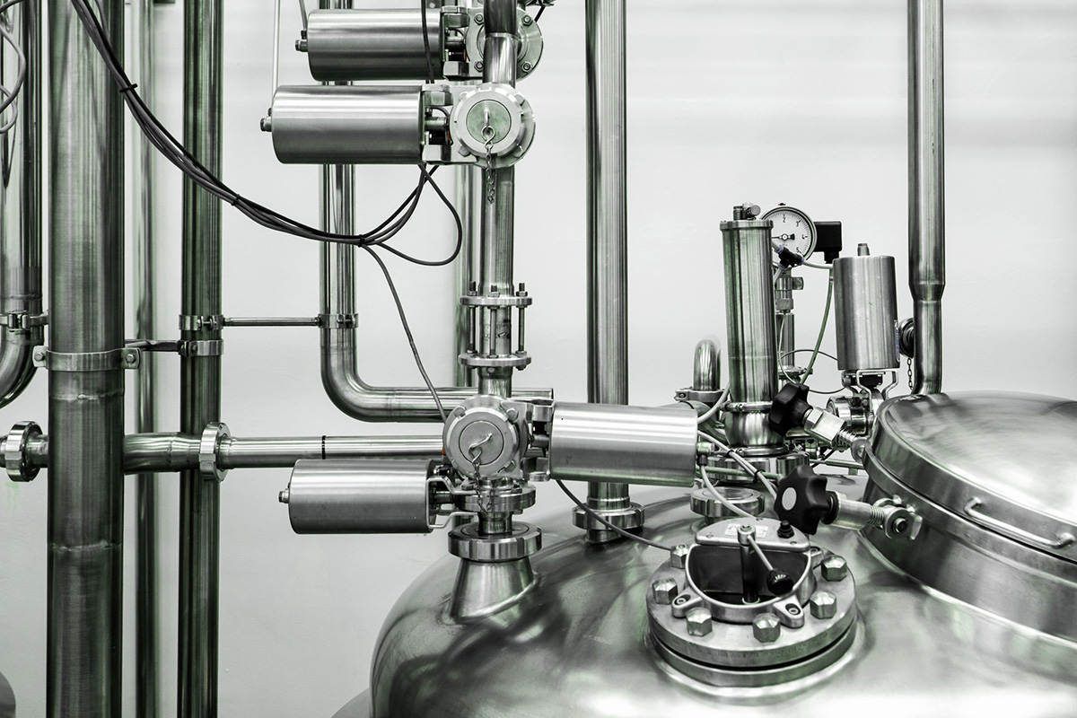 Detailaufnahme einer industriellen Edelstahlanlage mit Rohrleitungen, Ventilen, Druckmessgeräten und einem großen geschlossenen Behälter.